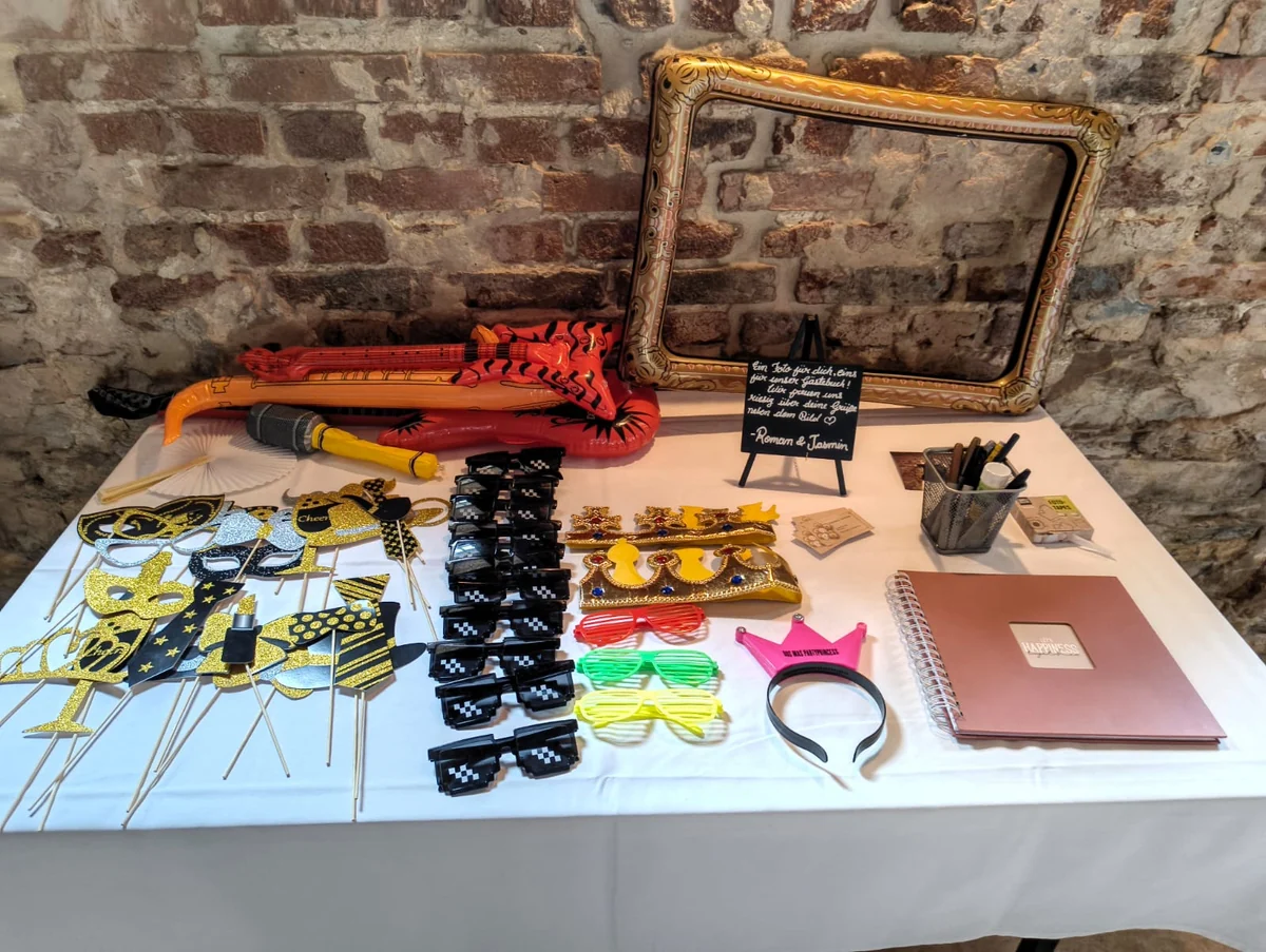 Fotoprops mit bunten Brillen, Schildern und Bilderrahmen sowie Gästebuch und Stiften.